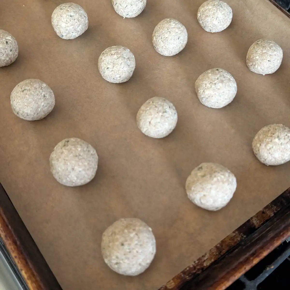 Uncooked Meatballs on Parchment and Baking Sheet